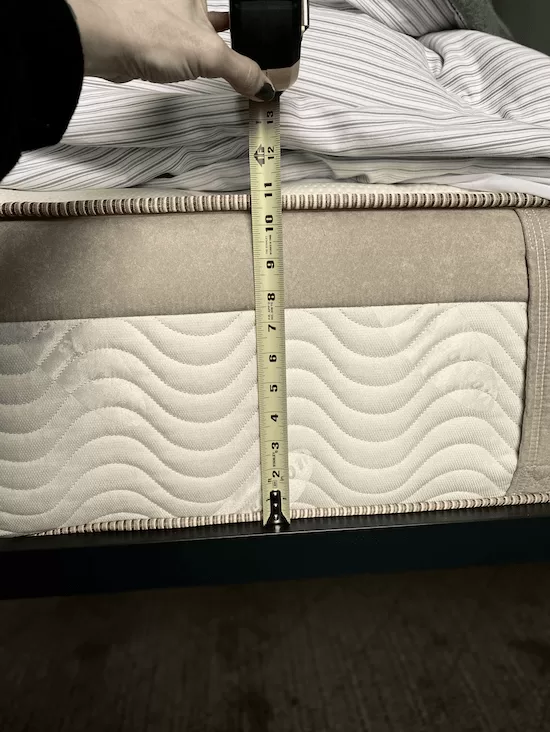 A measuring tape held up to the side of a mattress on a bed.