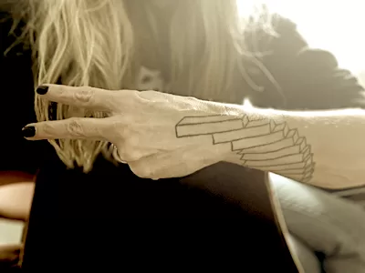 A forearm with a tattoo of mathematical harmony and the hand holding up two fingers